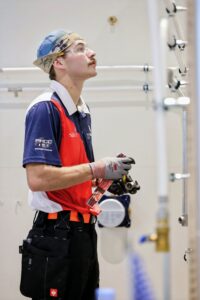 A technician in safety gear examines plumbing components while working on a pipe system.